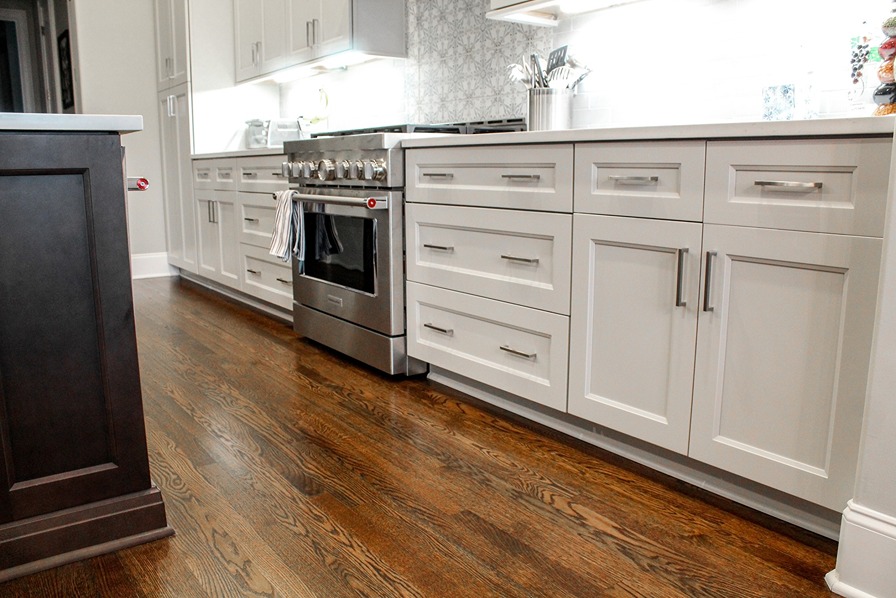 A finished white shaker cabinet run with a range and hardwood flooring
