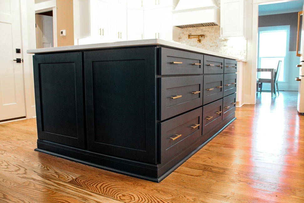 A black framed kitchen island built by Tiger Cabinetry, with brass drawer pulls on oak flooring
