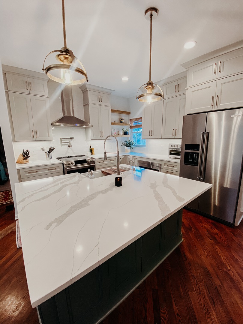 A Nashville kitchen with warm grey perimeter cabinets and a deep green island topped with veined marble under brass lantern pendants
