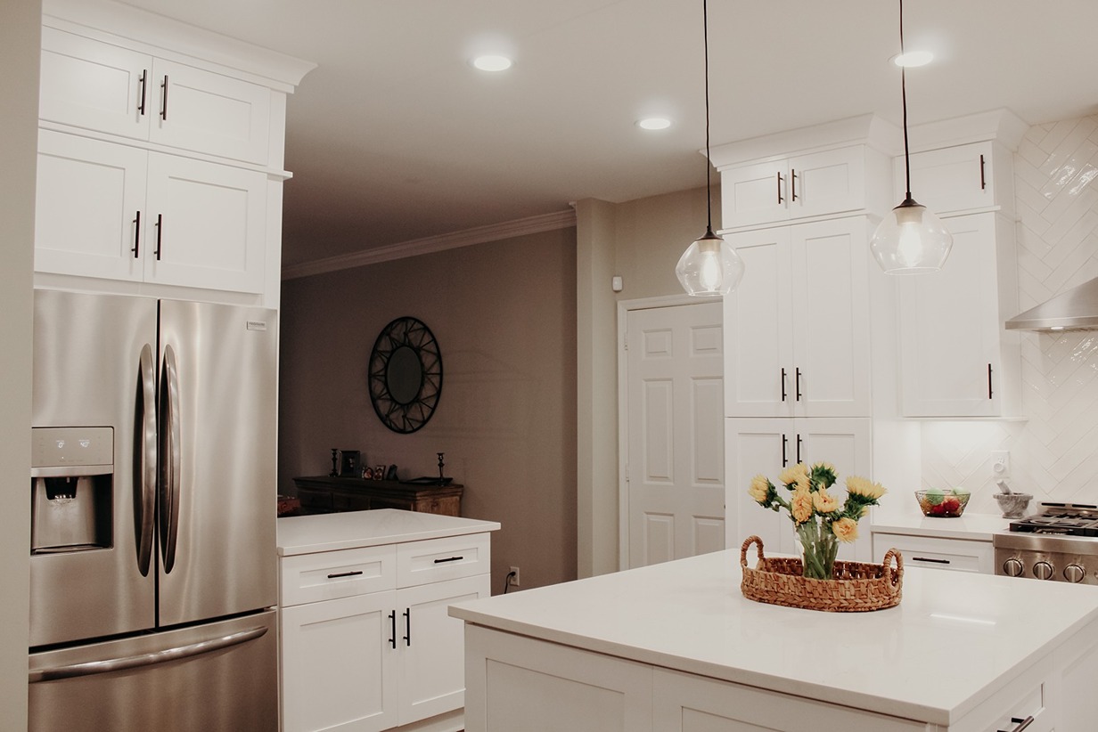 A white shaker kitchen with full height cabinetry, a herringbone tile backsplash and glass pendants over a stone island